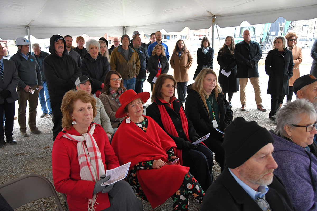 A small crowd under a tent to listen to ceremony. 