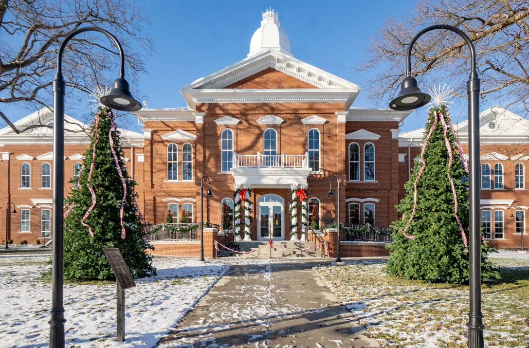 A large brick and white trim courthouse with two trees in front.